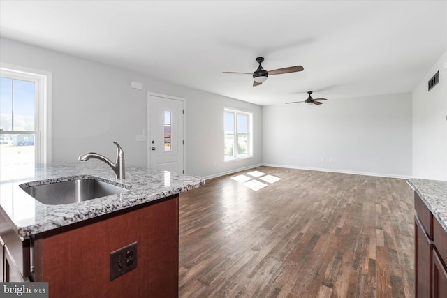 kitchen featuring dark hardwood / wood-style floors, light stone countertops, sink, and a kitchen island with sink