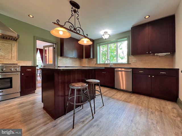 kitchen with light wood-type flooring, a center island, tasteful backsplash, hanging light fixtures, and appliances with stainless steel finishes