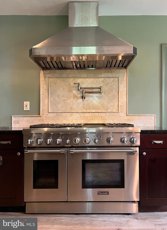 kitchen featuring high end range, dark brown cabinets, light hardwood / wood-style flooring, wall chimney exhaust hood, and decorative backsplash