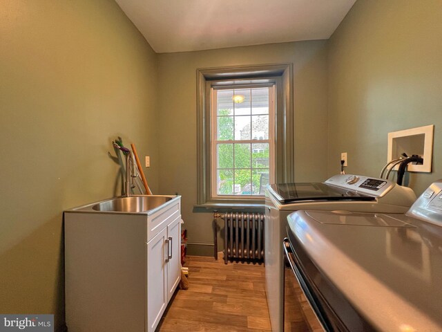 laundry area with sink, radiator heating unit, washer and clothes dryer, cabinets, and light wood-type flooring