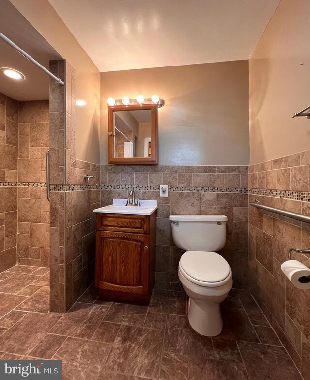 bathroom with tile walls, a tile shower, vanity, and toilet