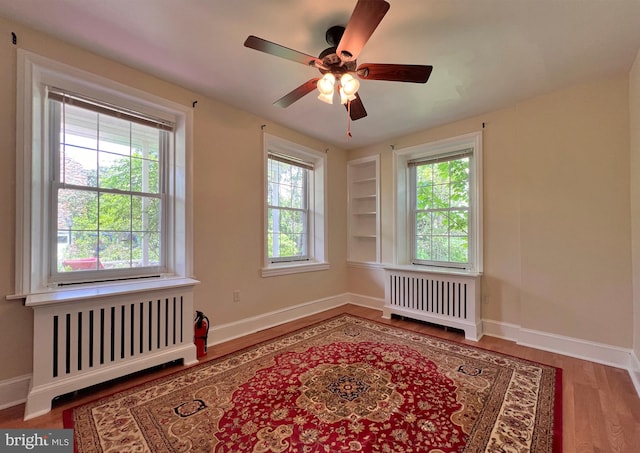 unfurnished room featuring a wealth of natural light, ceiling fan, radiator, and hardwood / wood-style flooring