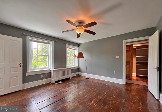 unfurnished bedroom featuring a spacious closet, dark hardwood / wood-style flooring, radiator heating unit, a closet, and ceiling fan