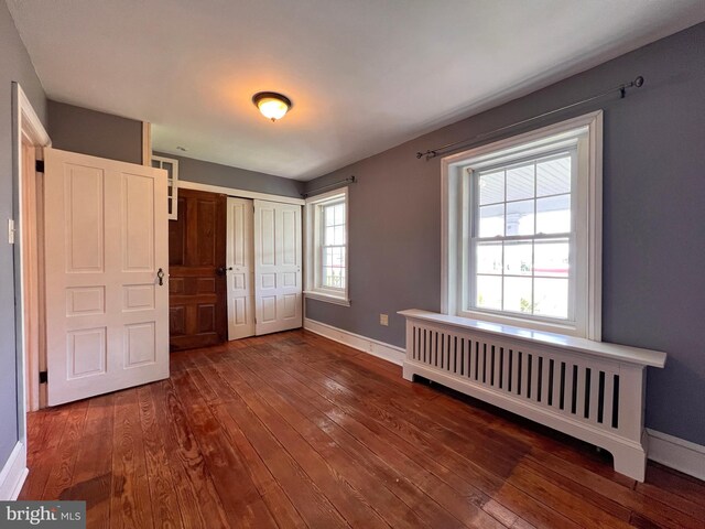 unfurnished bedroom featuring radiator and dark hardwood / wood-style flooring