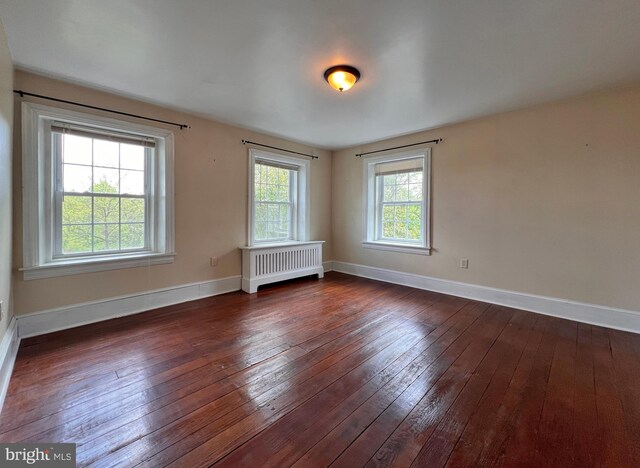 empty room with dark hardwood / wood-style floors, radiator heating unit, and a wealth of natural light