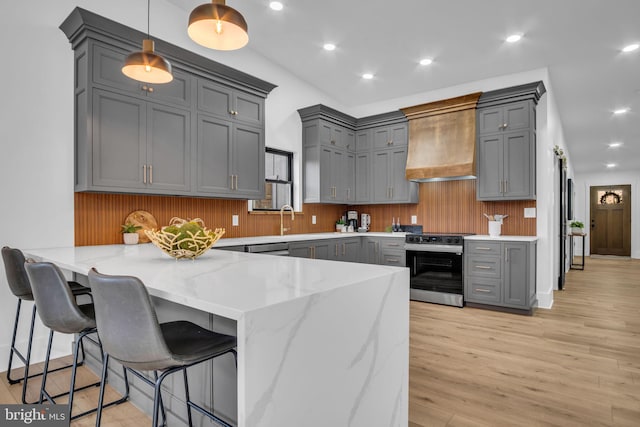 kitchen featuring gray cabinets, custom range hood, hanging light fixtures, stainless steel range oven, and a peninsula