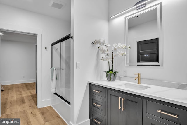 full bathroom featuring shower / bath combination with glass door, visible vents, vanity, wood finished floors, and baseboards