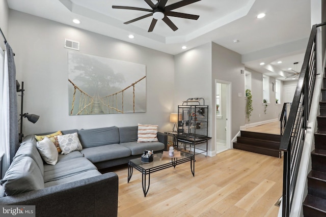 living room with a tray ceiling, ceiling fan, and light wood-type flooring