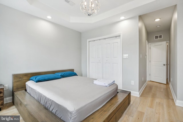 bedroom featuring a notable chandelier, a closet, a raised ceiling, and light hardwood / wood-style flooring