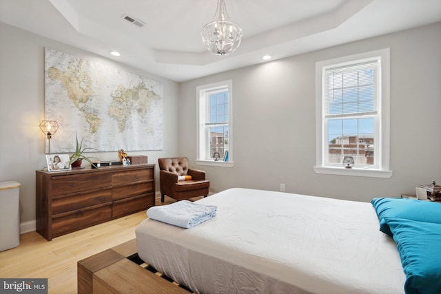 bedroom with an inviting chandelier, light wood-type flooring, and a tray ceiling