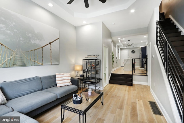 living room with a tray ceiling, ceiling fan, and light wood-type flooring