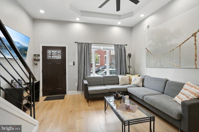 living room featuring a tray ceiling, ceiling fan, light hardwood / wood-style flooring, and a towering ceiling