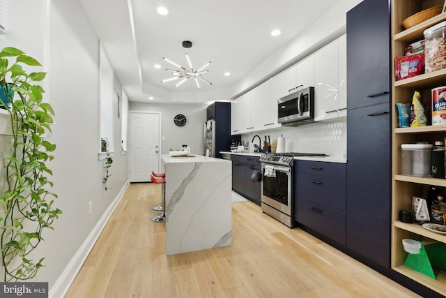 kitchen with white cabinetry, an inviting chandelier, appliances with stainless steel finishes, a kitchen island, and light wood-type flooring