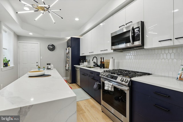 kitchen featuring white cabinets, sink, light hardwood / wood-style flooring, appliances with stainless steel finishes, and a chandelier