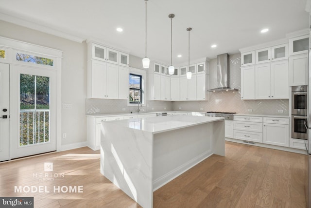 kitchen featuring white cabinets, wall chimney exhaust hood, a center island, and light hardwood / wood-style flooring