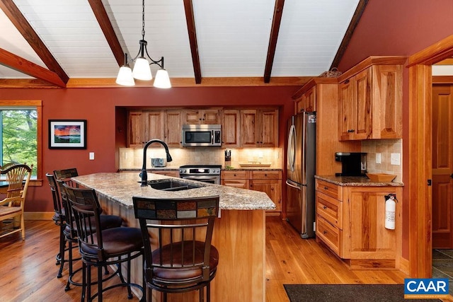 kitchen featuring light hardwood / wood-style floors, hanging light fixtures, a kitchen island with sink, vaulted ceiling with beams, and appliances with stainless steel finishes