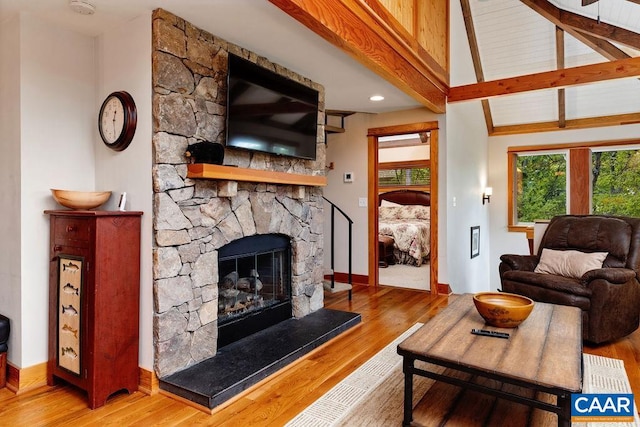 living room featuring wood-type flooring, a stone fireplace, and lofted ceiling with beams