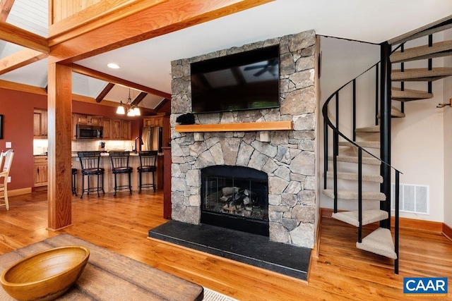 living room featuring a stone fireplace, beam ceiling, and hardwood / wood-style flooring