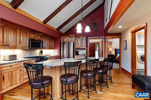 kitchen featuring hanging light fixtures, beamed ceiling, an island with sink, and appliances with stainless steel finishes