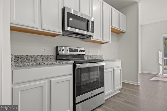 kitchen featuring white cabinets, appliances with stainless steel finishes, light wood-type flooring, and light stone counters