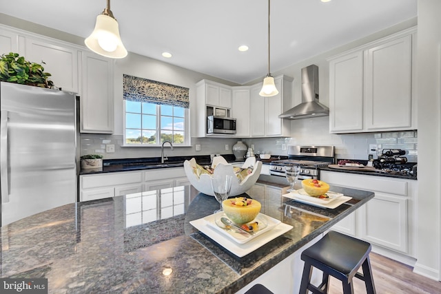 kitchen featuring white cabinetry, wall chimney exhaust hood, stainless steel appliances, and decorative light fixtures