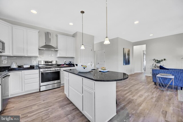 kitchen with stainless steel gas range oven, wall chimney exhaust hood, white cabinetry, a kitchen island, and hanging light fixtures