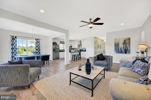 living room featuring ceiling fan with notable chandelier and light wood-type flooring