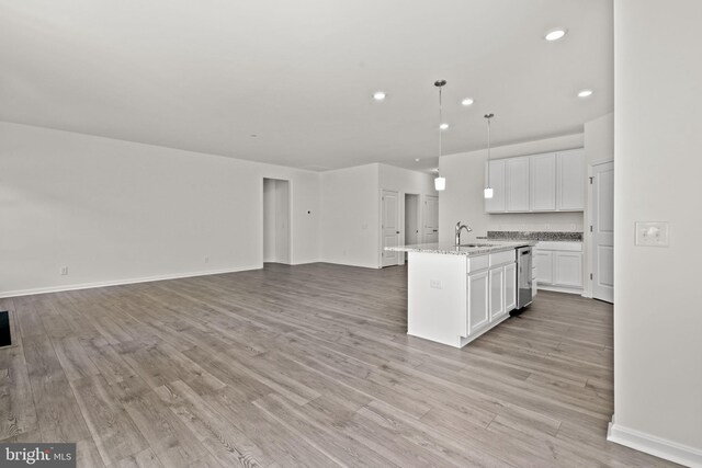 kitchen featuring light stone counters, sink, pendant lighting, white cabinetry, and an island with sink