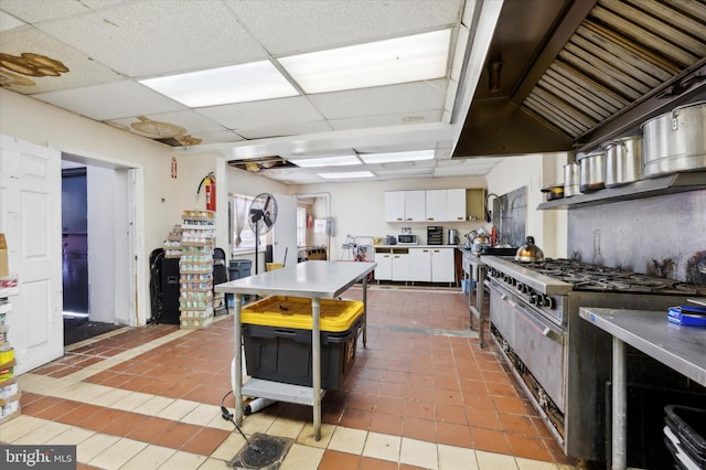 kitchen featuring stainless steel range, a paneled ceiling, light tile floors, white cabinets, and a kitchen bar