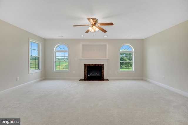 unfurnished living room with a high end fireplace, light carpet, and ceiling fan