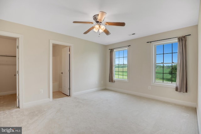 unfurnished bedroom with light carpet, ensuite bathroom, a walk in closet, ceiling fan, and a closet