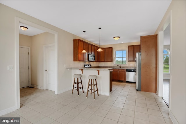 kitchen with hanging light fixtures, stainless steel appliances, kitchen peninsula, a kitchen bar, and light tile patterned floors