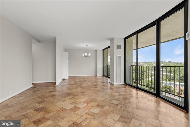 spare room featuring light parquet floors, an inviting chandelier, and expansive windows