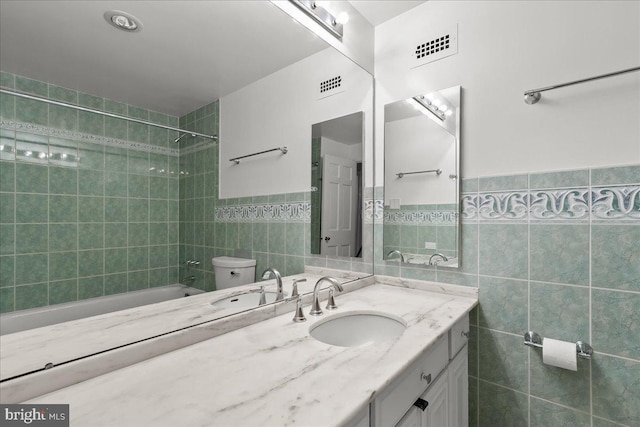 full bathroom featuring vanity, toilet, tile walls, and tiled shower / bath combo