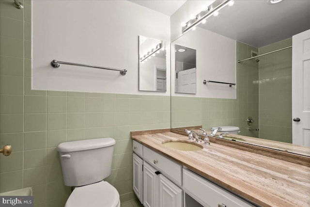 bathroom featuring vanity, toilet, a tile shower, and tile walls