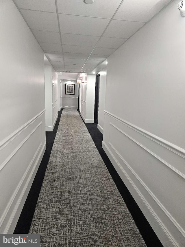 corridor featuring dark colored carpet and a paneled ceiling