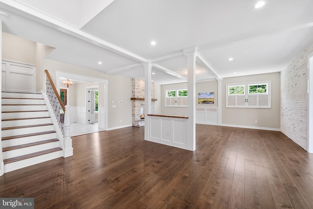 unfurnished living room with beamed ceiling, dark hardwood / wood-style flooring, a fireplace, and ornate columns