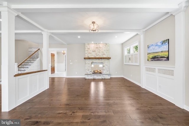 unfurnished living room featuring a stone fireplace, dark hardwood / wood-style flooring, beamed ceiling, and ornate columns