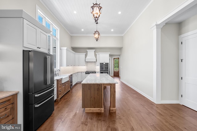 kitchen with high end fridge, wood-type flooring, custom range hood, a kitchen island, and white cabinets