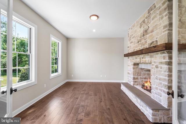 unfurnished living room with a stone fireplace, french doors, and dark wood-type flooring