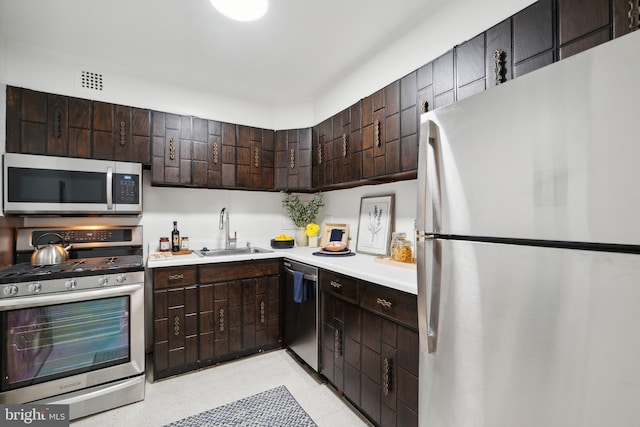 kitchen featuring dark brown cabinetry, sink, light tile flooring, and appliances with stainless steel finishes