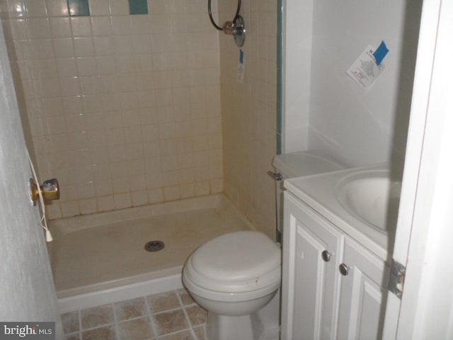 bathroom featuring a tile shower, tile flooring, vanity, and toilet