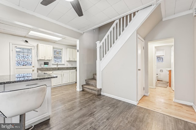 kitchen featuring white cabinetry, ornamental molding, dark stone counters, and light hardwood / wood-style flooring