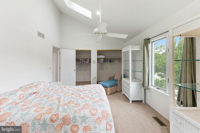 carpeted bedroom featuring ceiling fan, multiple windows, a skylight, and multiple closets