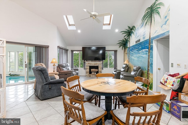 tiled dining space with high vaulted ceiling, a fireplace, ceiling fan, and a skylight