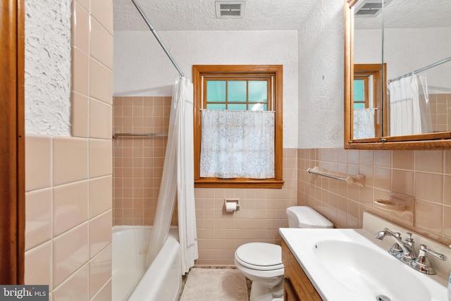 full bathroom with vanity, toilet, a textured ceiling, tile walls, and shower / tub combo