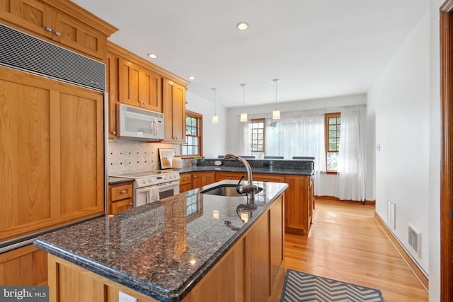 kitchen with a center island with sink, pendant lighting, white appliances, and sink