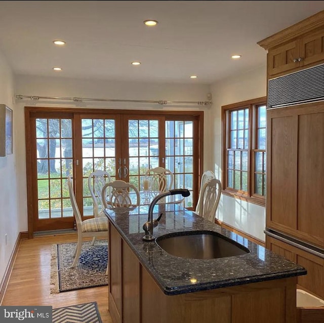 kitchen featuring sink, light wood-type flooring, an island with sink, and dark stone counters