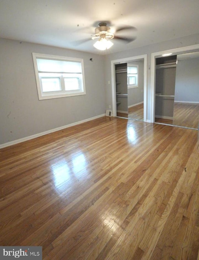 unfurnished bedroom featuring ceiling fan, wood-type flooring, and two closets