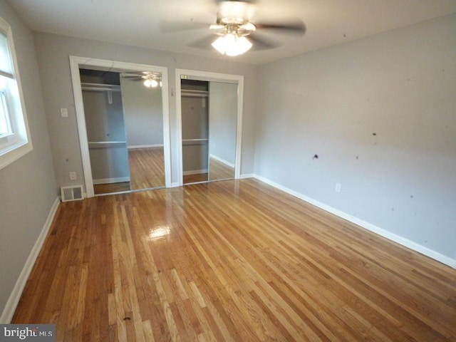 unfurnished bedroom featuring hardwood / wood-style flooring, ceiling fan, and multiple closets